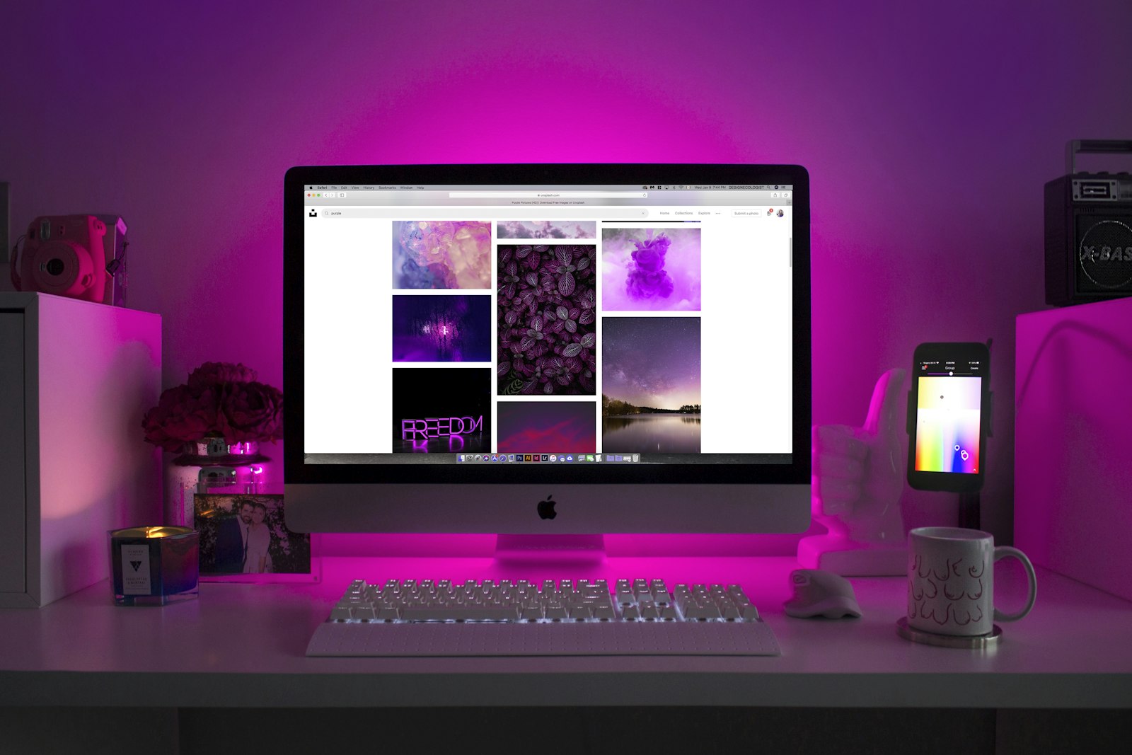 A desktop monitor on a magenta-lit desk showing a grid of photographs
